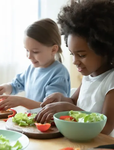 two young girls sitting at a table with plates of food
