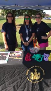Three female staff members pose behind outdoor booth table