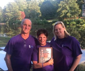 Man, woman holding portrait of soldier, and another woman pose in front of front of pond