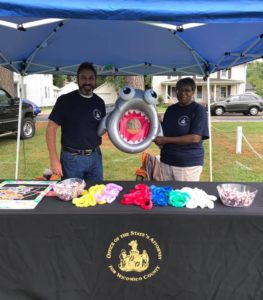 Man and woman staff holding an inflatable shark at National Night Out booth