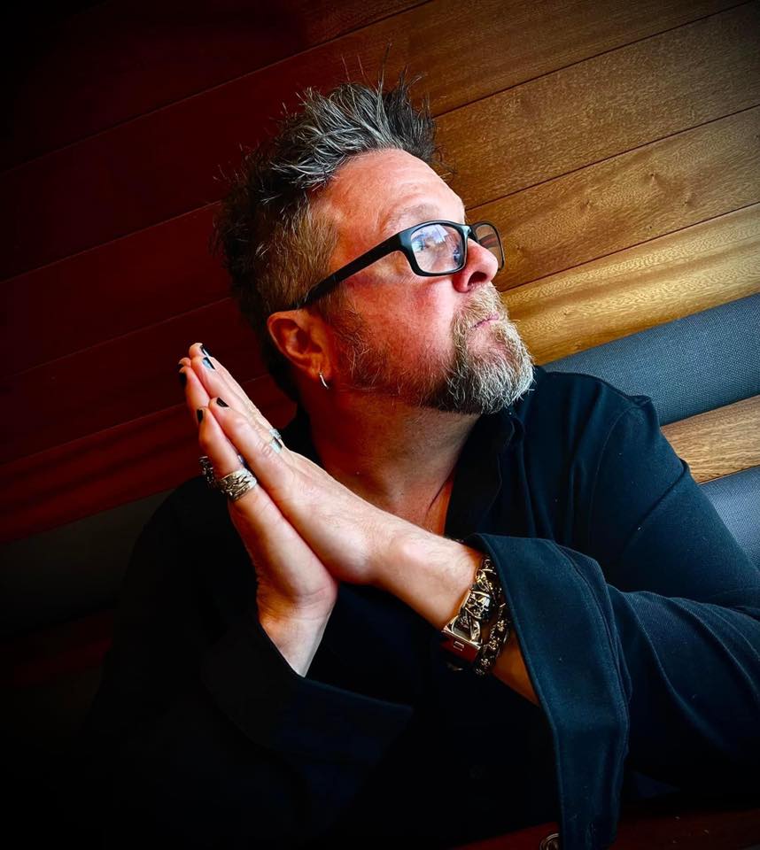 Profile headshot of a man with his hands together with black nail polish