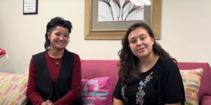 two women are sitting on a pink couch