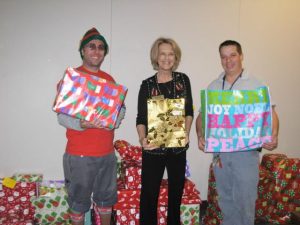 man with elf hat holding gifts with two others with gifts